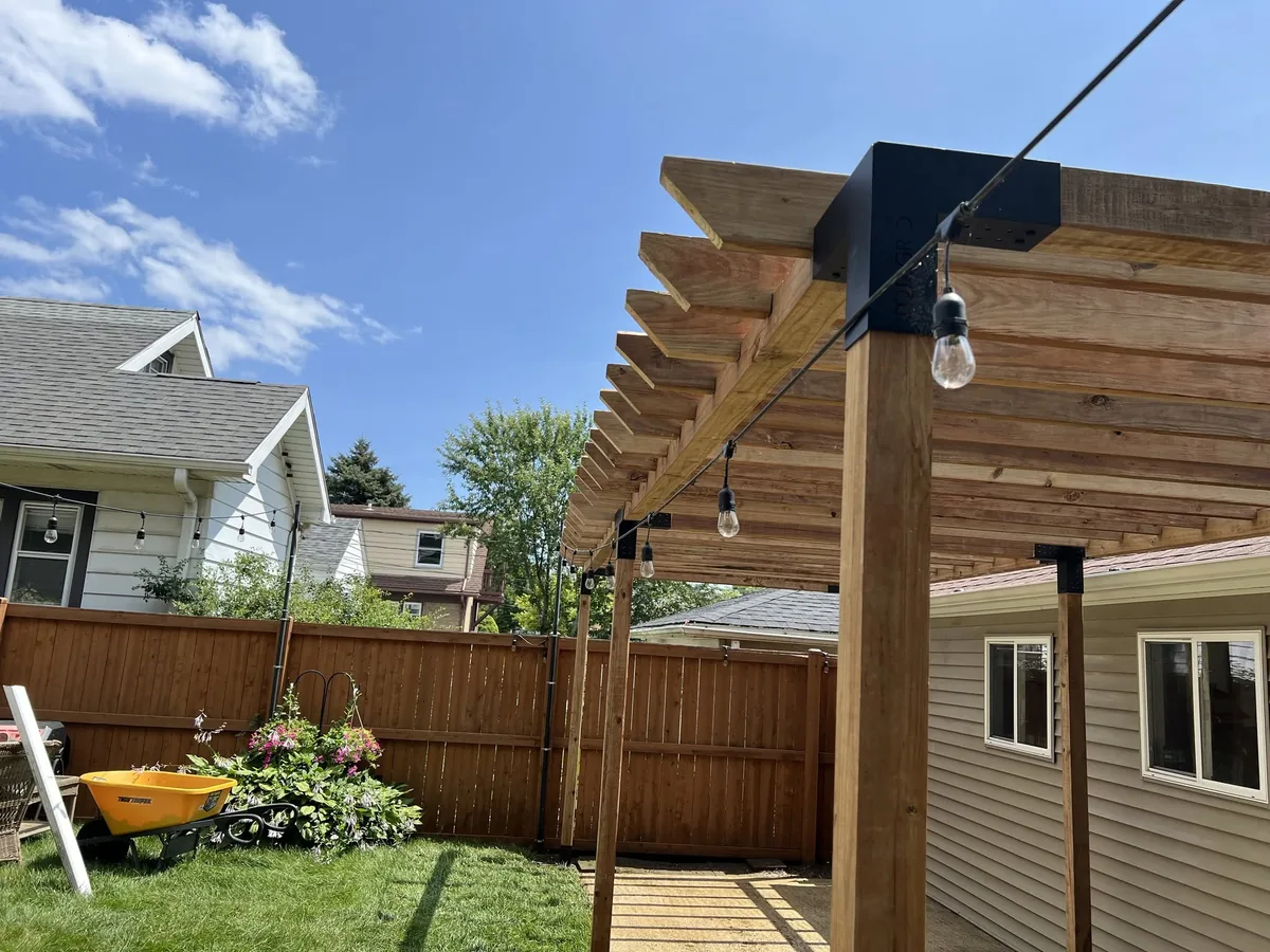 Backyard pergola built beside a privacy fence with string lights overhead