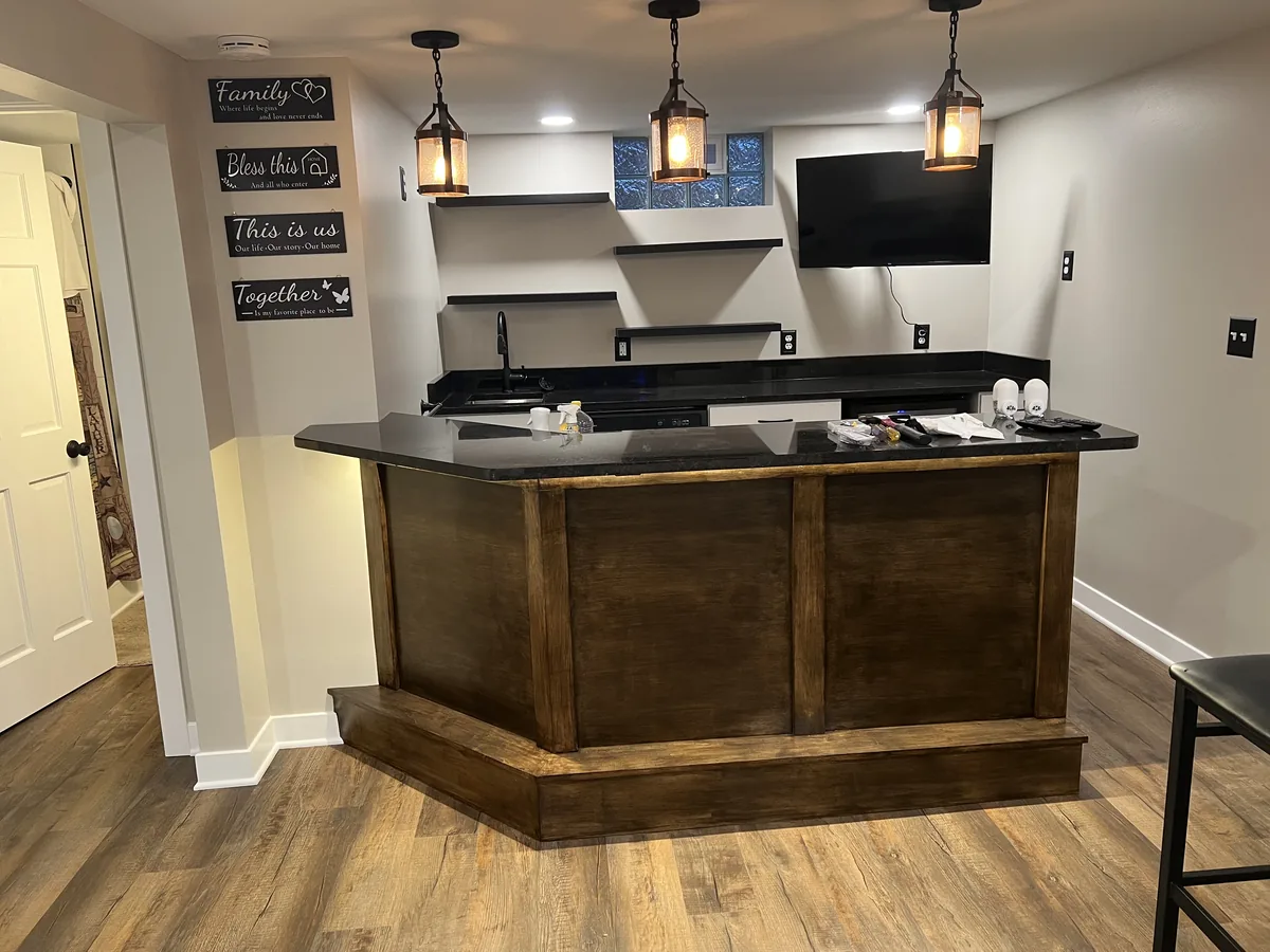 Custom basement bar with a dark wood base, stone counter and pendant lighting