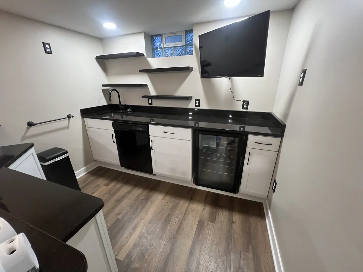 Basement bar with open shelving, a wall mounted television and beverage fridge