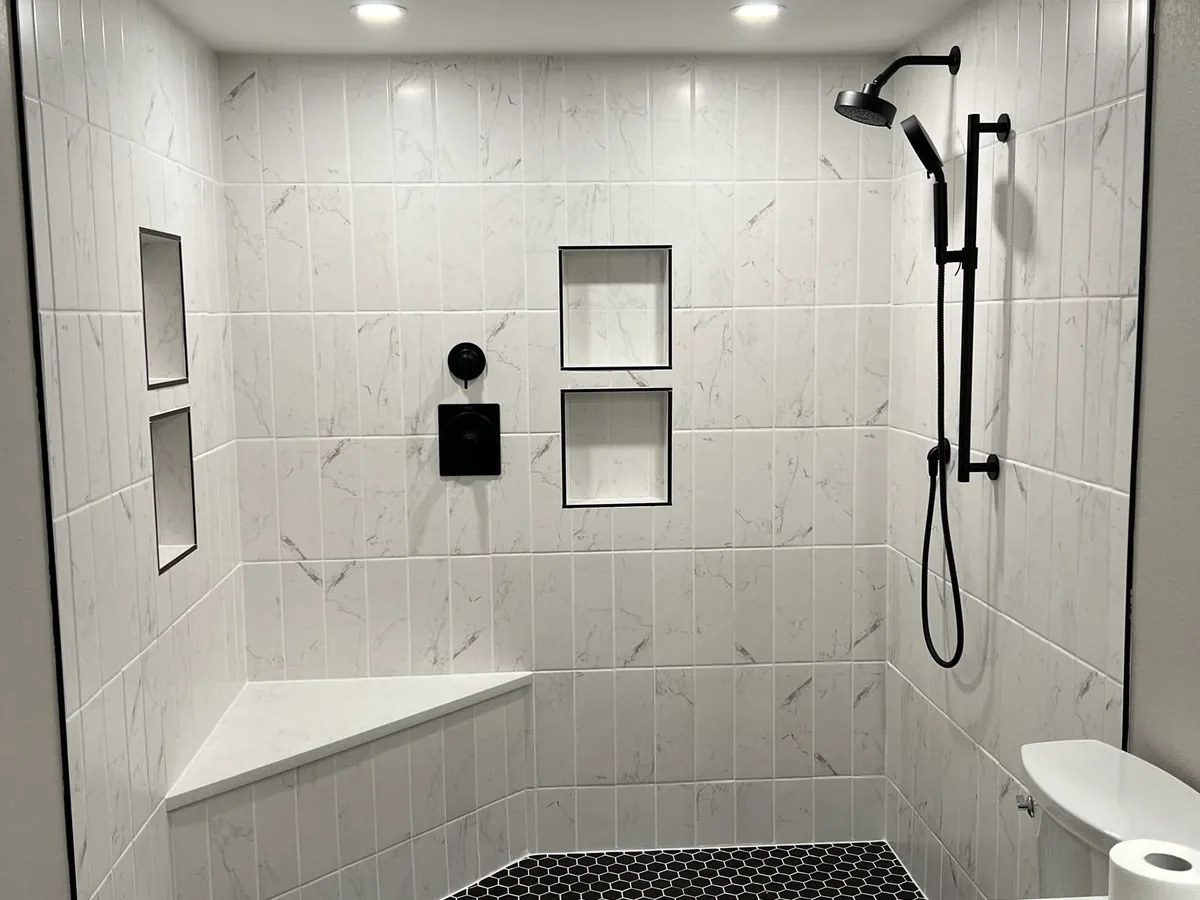 Finished walk in shower with white tile walls, black fixtures and a built in bench