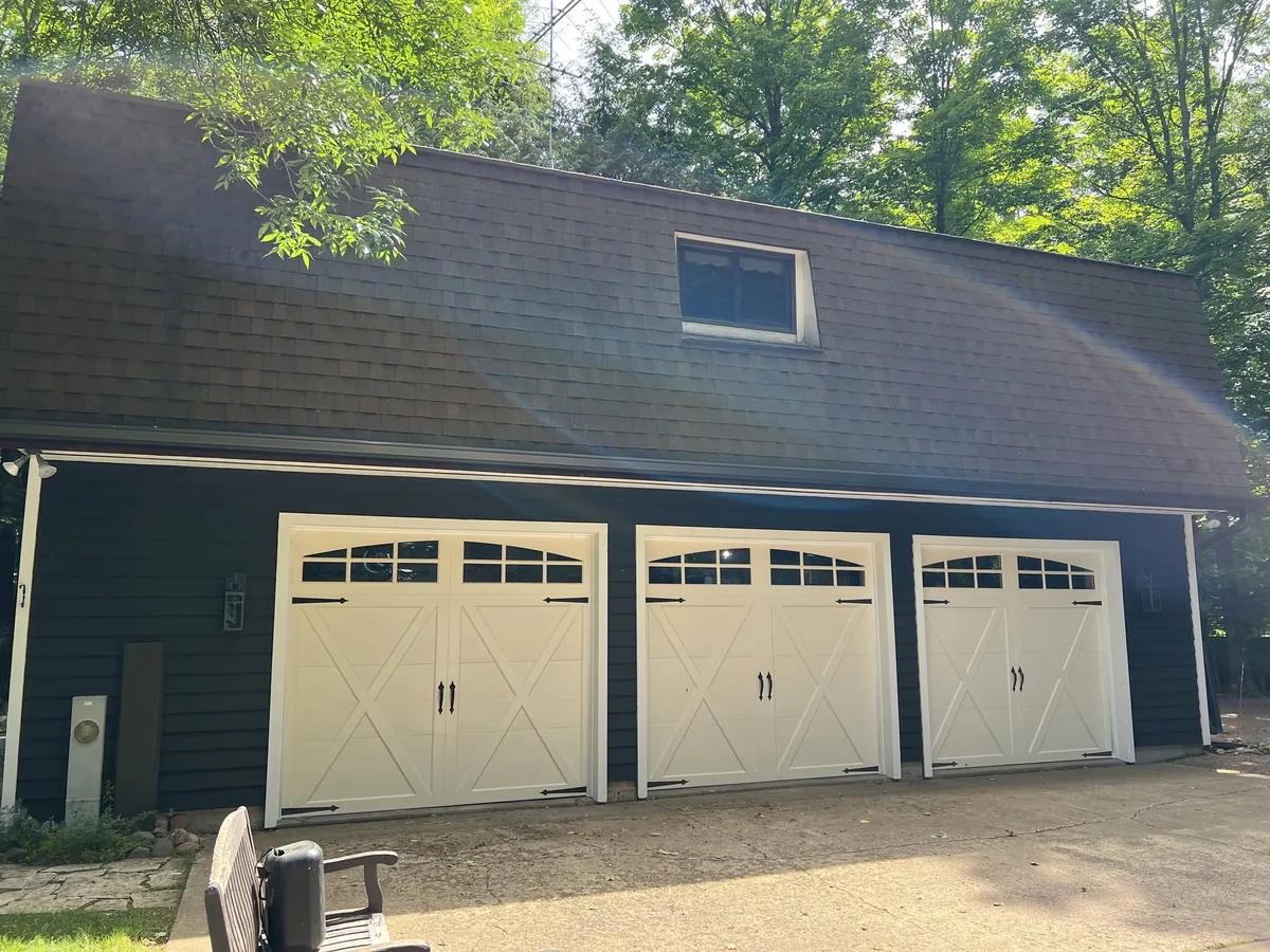 Detached three bay garage with a gambrel roof and white carriage style doors