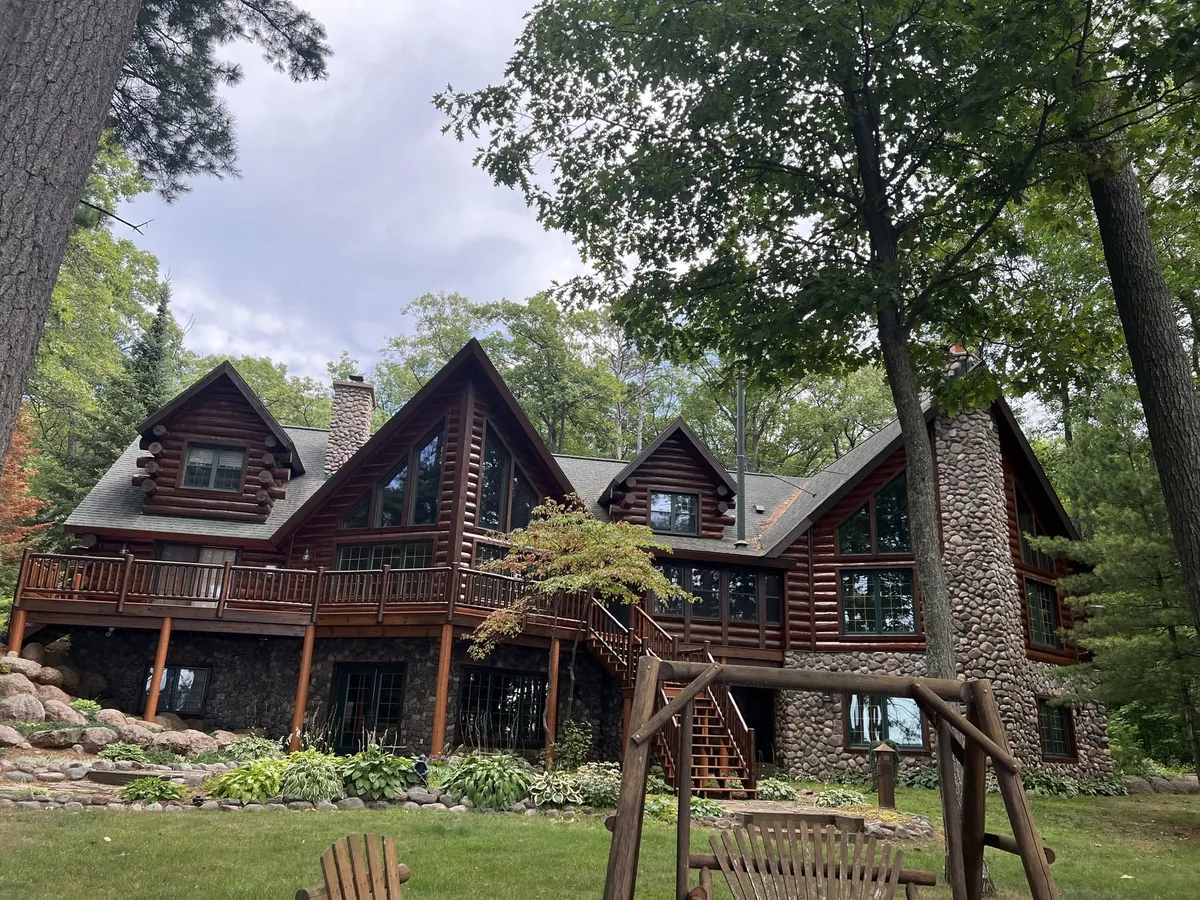Front elevation of a large log home with a stone chimney and pine trees