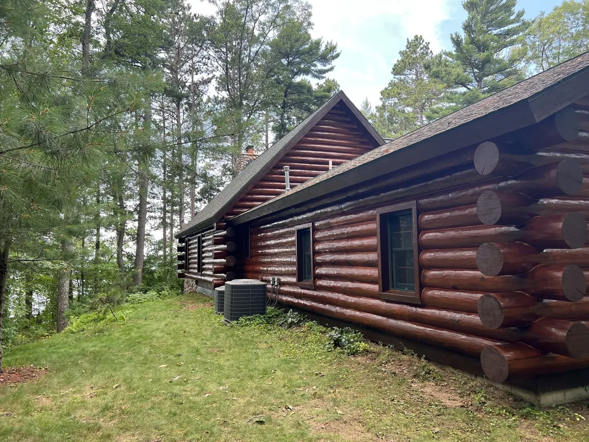 Side elevation of a log home with a mowed lawn and wooded lot