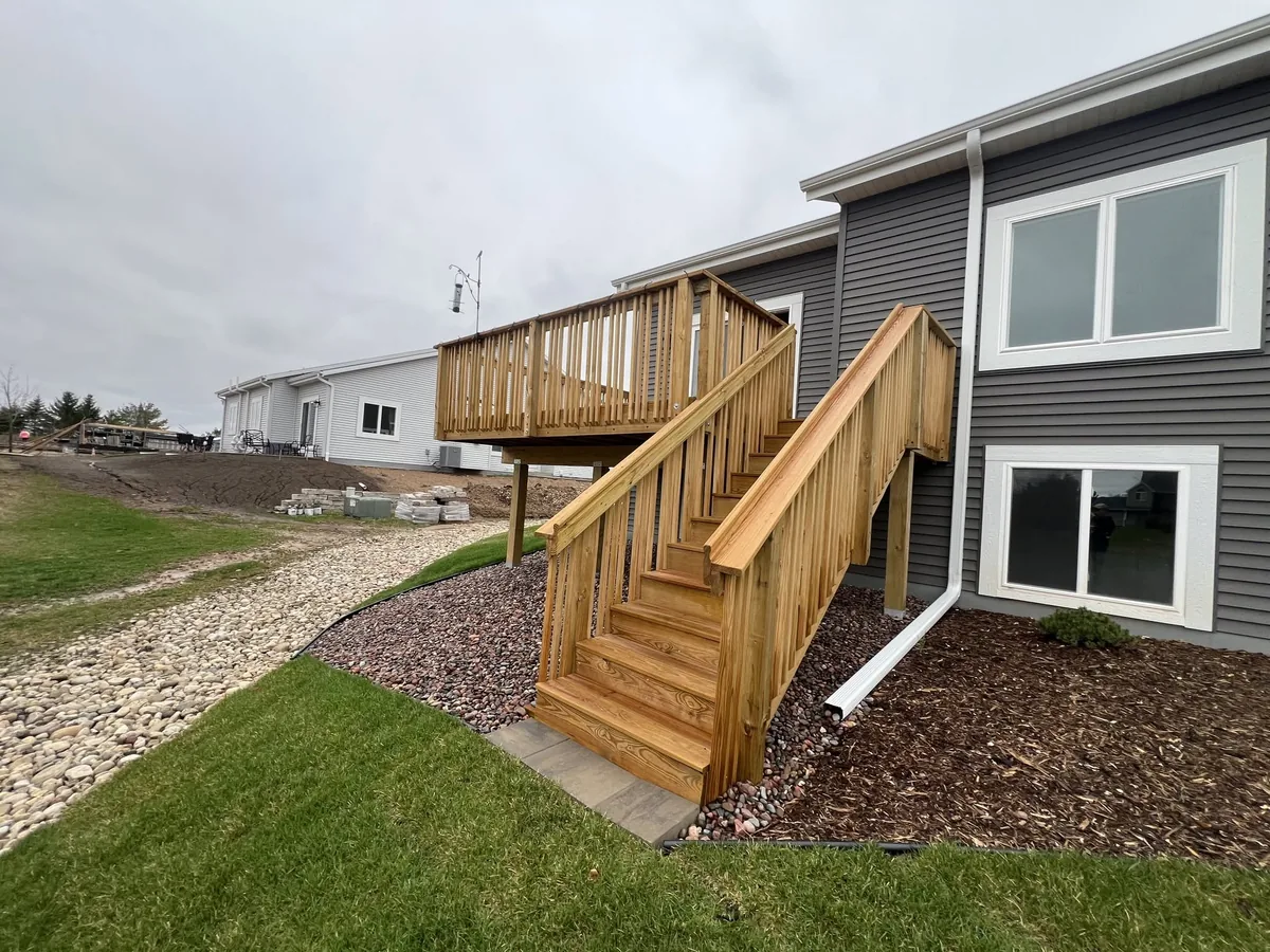 New cedar deck and stairway attached to a gray sided home with rock landscaping