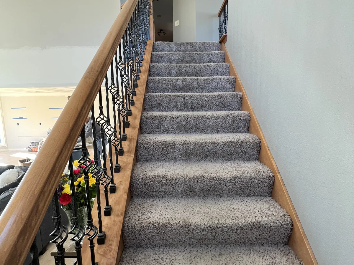 Staircase with a carpeted tread runner, wood handrail and iron balusters before the remodel