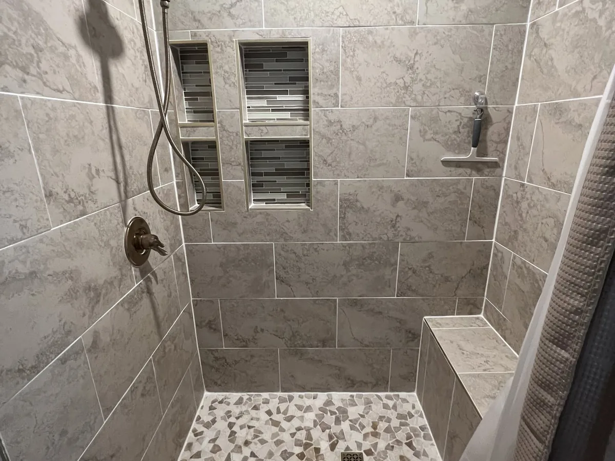 Walk in shower with gray tile walls, a mosaic accent niche and a pebble floor