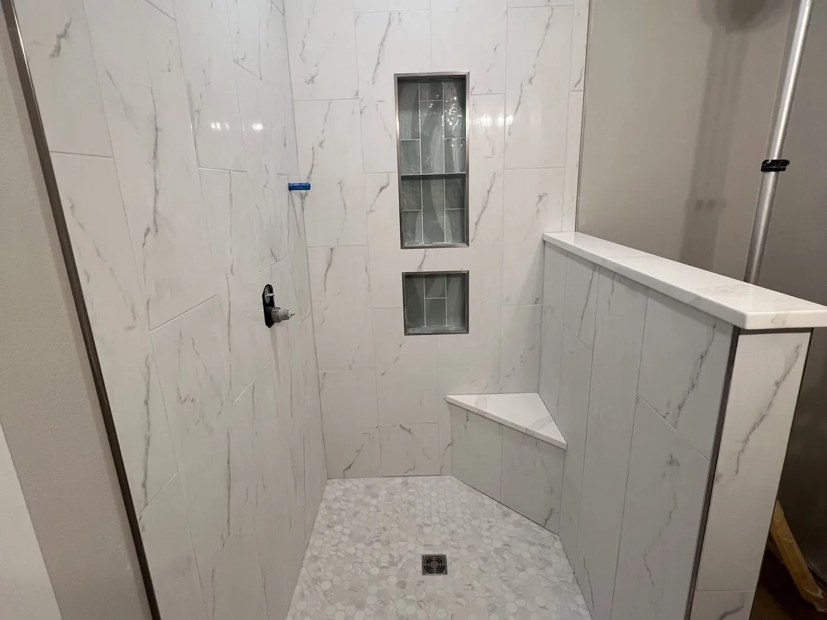 Walk in shower finished in large format marble look tile with a glass block window