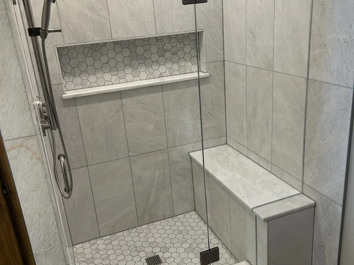 Walk in shower with marble look tile, a built in bench and a mosaic accent niche