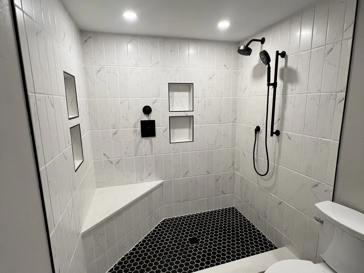 Finished walk in shower with white tile walls, black fixtures and a black hex tile floor